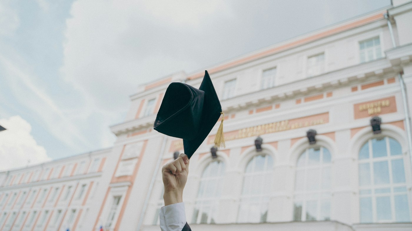 A PGDE graduate holding a cap outside a university that awards postgraduate diplomas in education