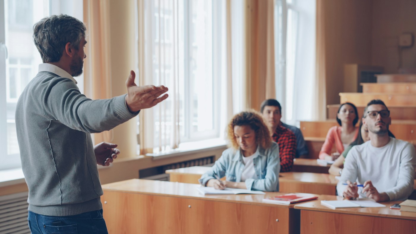 QTLS or QTS compared as a further education teacher works with adult learners in a classroom