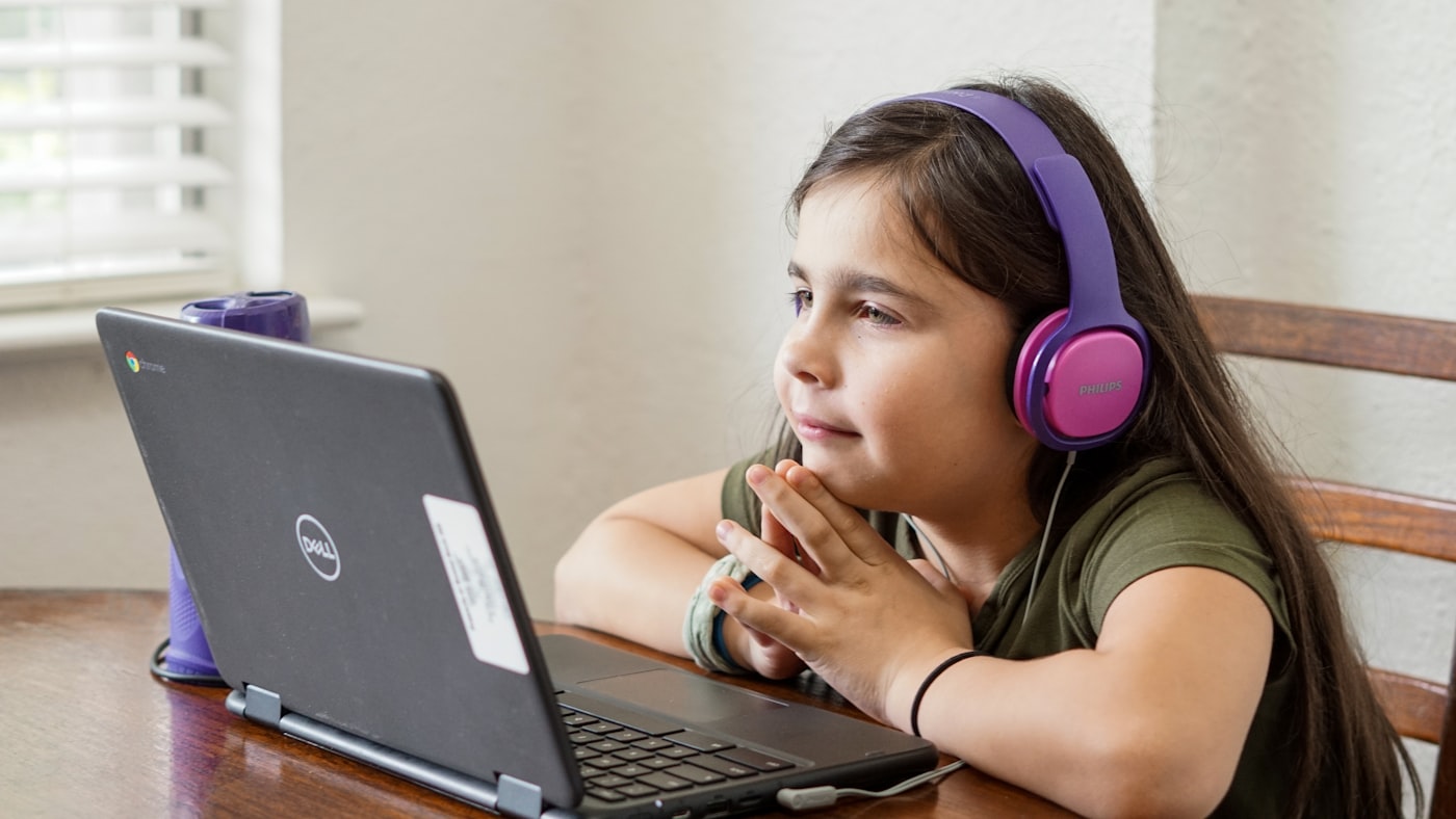Young girl at a table taking an online English lesson for kids on a laptop