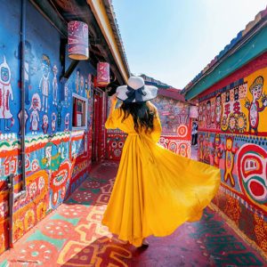 Woman wearing a yellow dress walking down a street with decorative murals on either side of her